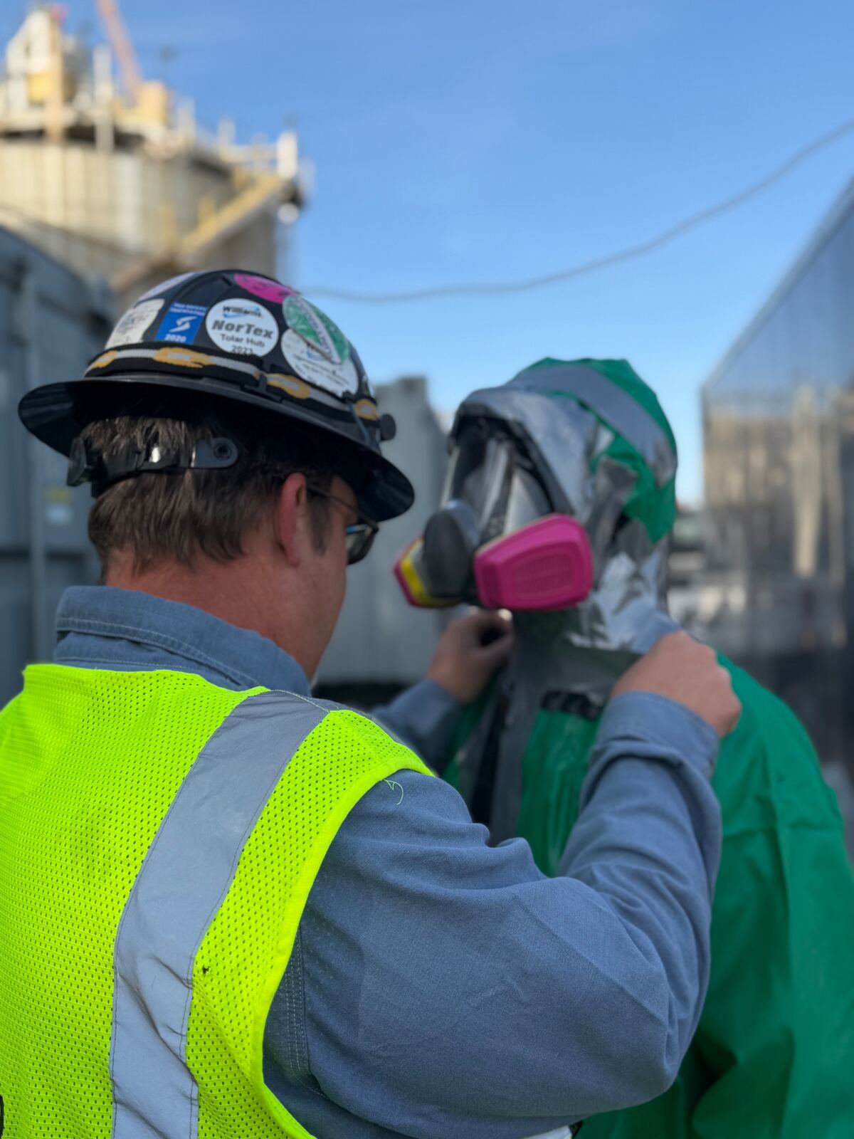 AIT supervisor performing PPE inspection on a technician in encapsulating chemical suit and full-face respirator
